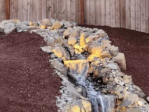 Rock drainage creek bed with yellow accent stones and natural boulders on mulch base