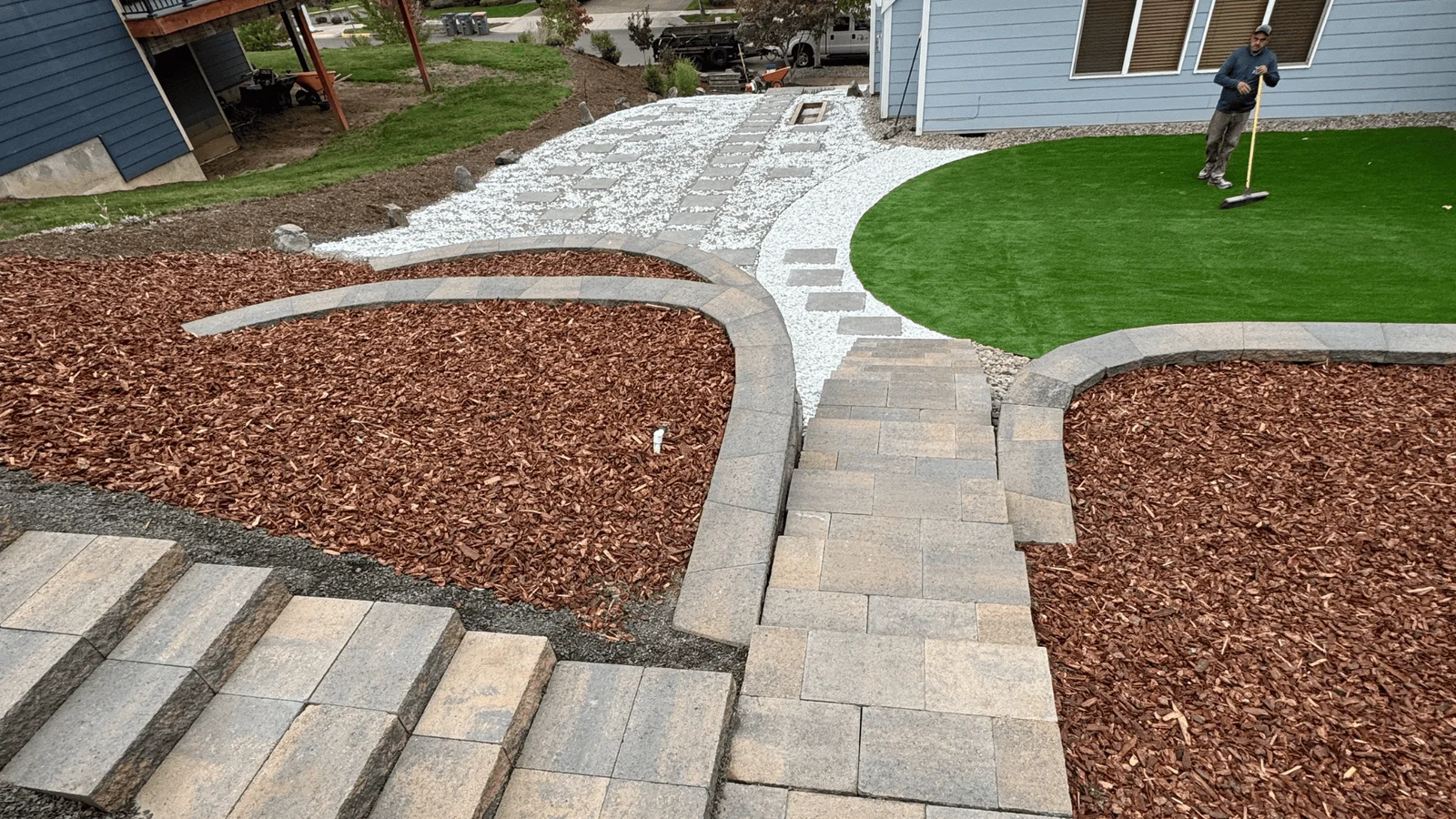 Paver patio with curved edging, mulch beds, and artificial turf lawn in residential backyard