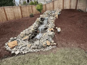 Stacked stone and boulder landscape feature with river rock accents in mulched garden bed