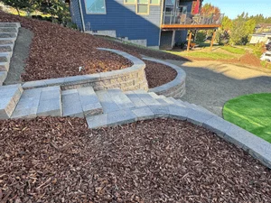 Curved concrete paver patio with curved retaining wall and river rock mulch landscaping