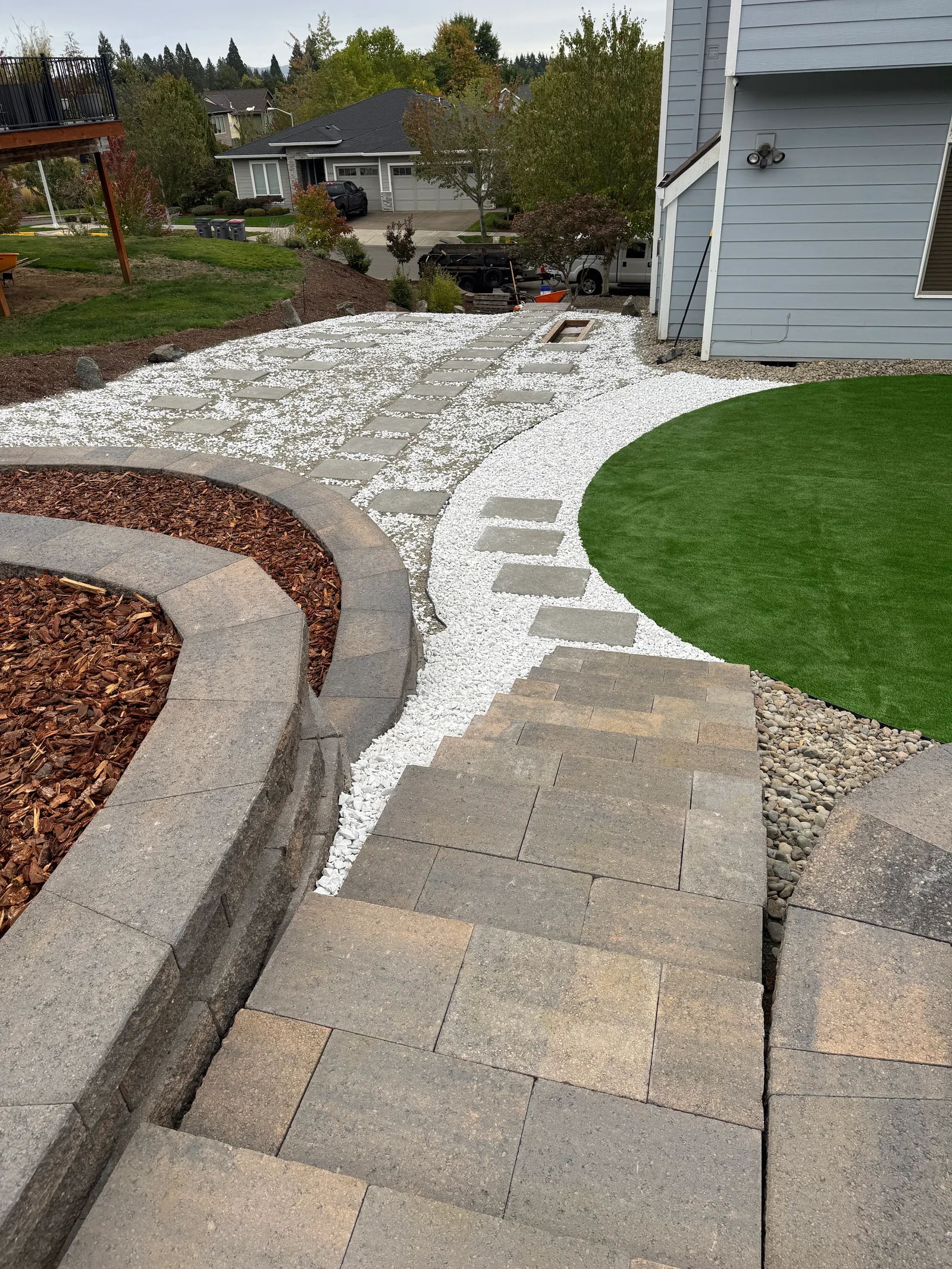Paver patio with tumbled concrete pavers, white river rock, artificial turf, and curved retaining walls