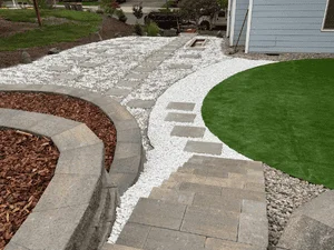 Curved gray paver patio with gravel borders and mulched landscape beds