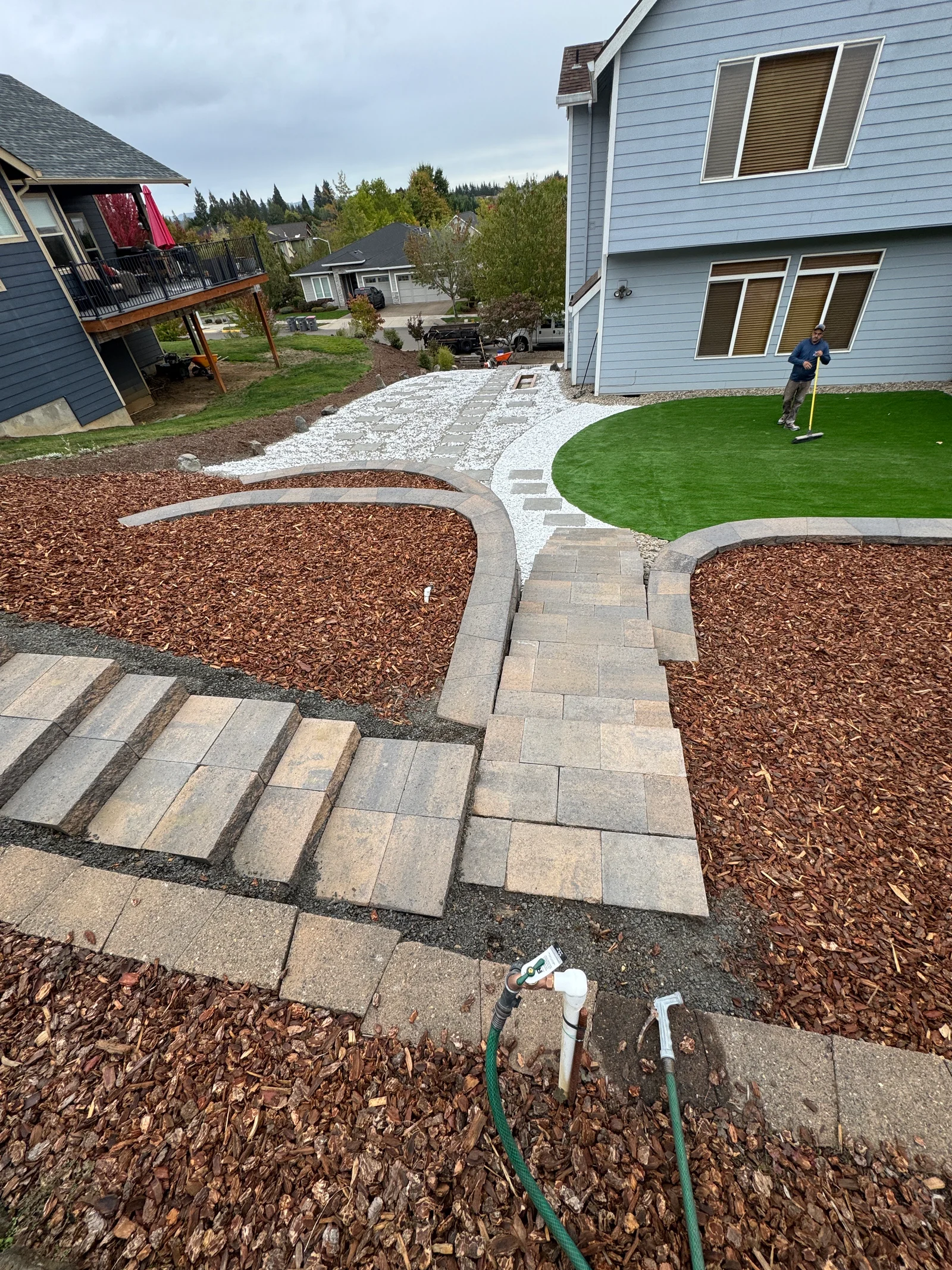 Paver patio with curved edging, artificial turf, mulch beds, and gravel accents in residential backyard