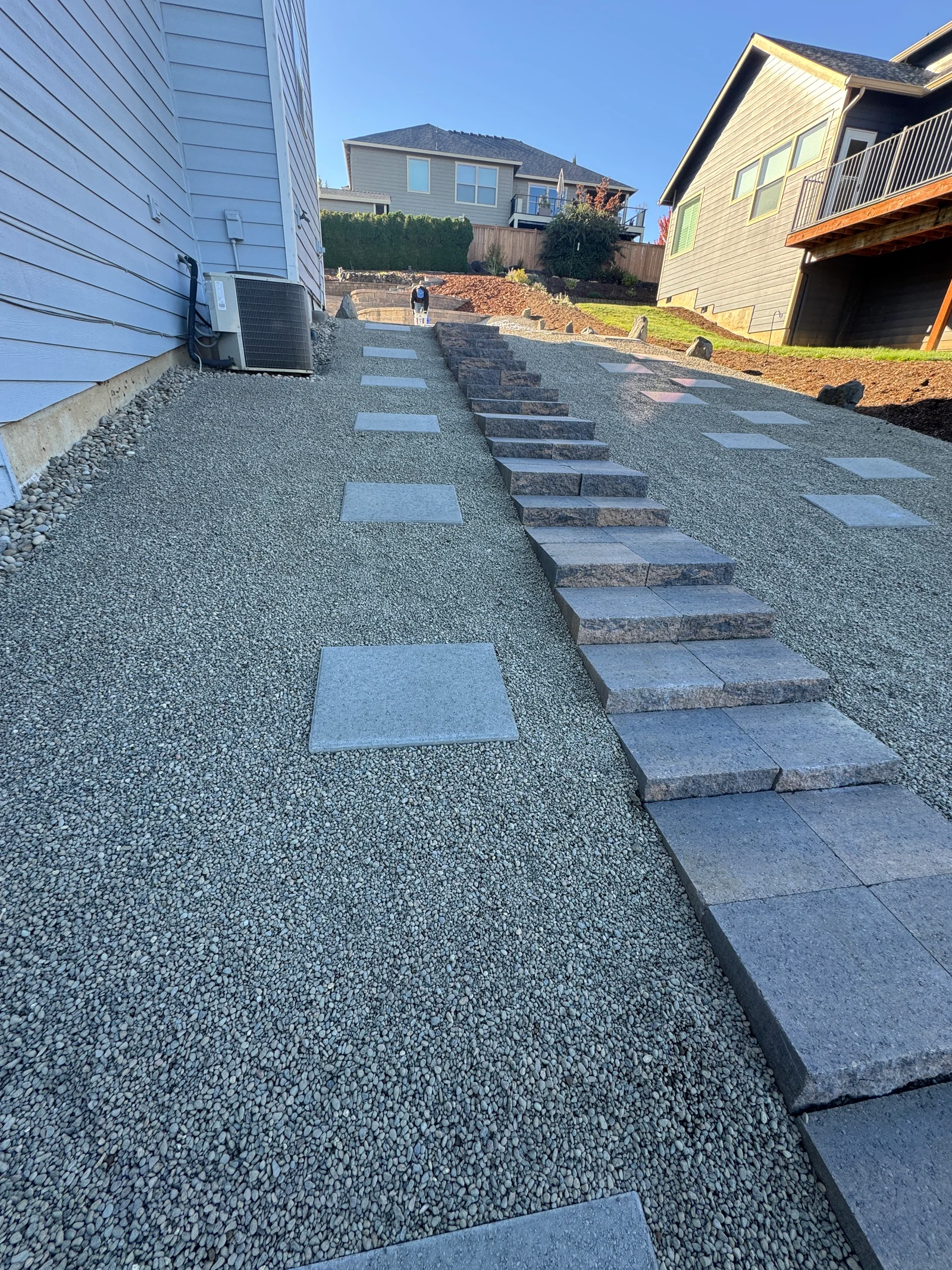 Gray pavers and natural stone steps on gravel base leading uphill between residential homes