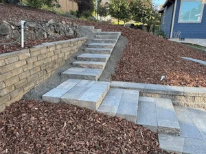 Concrete slab pathway with retaining wall and mulch landscaping on sloped terrain