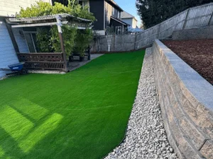 Artificial turf lawn with stacked stone retaining wall and white rock edging