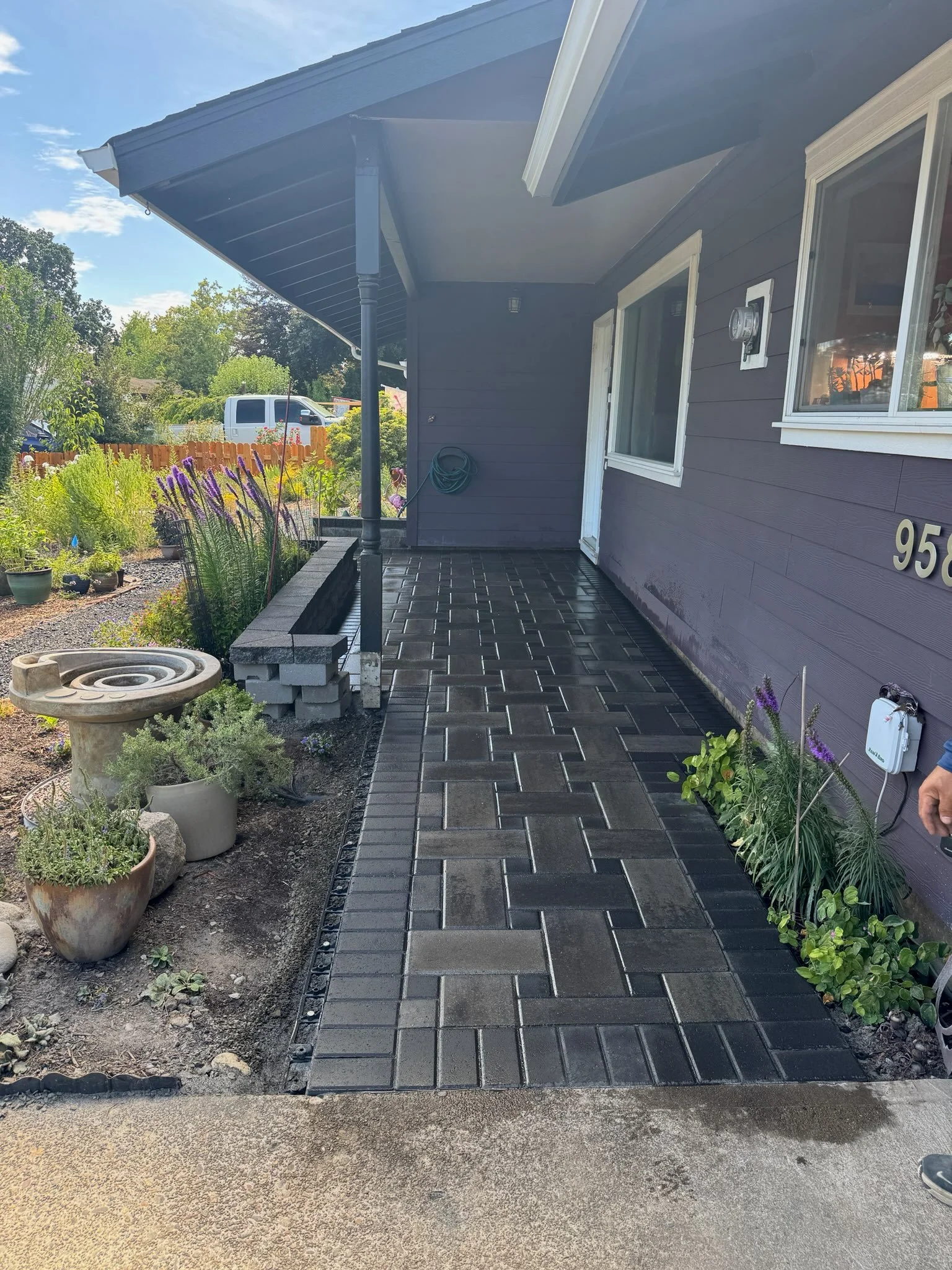Dark gray paver walkway with pergola shade structure and landscape plantings