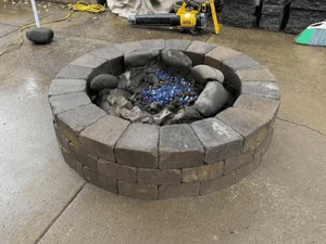 Circular stone fire pit with stacked paver ring and blue glass fire media insert