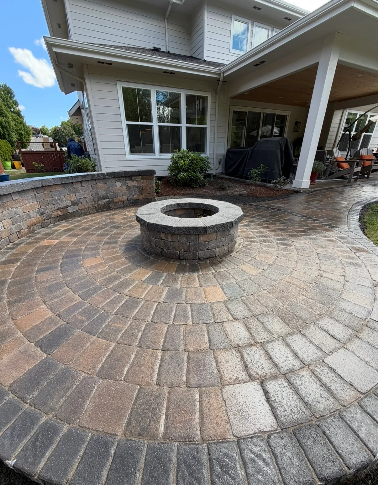 Circular paver patio with radial pattern and central stone fire pit, retaining wall border