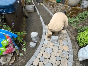 Worker installing concrete pavers in running bond pattern for patio base