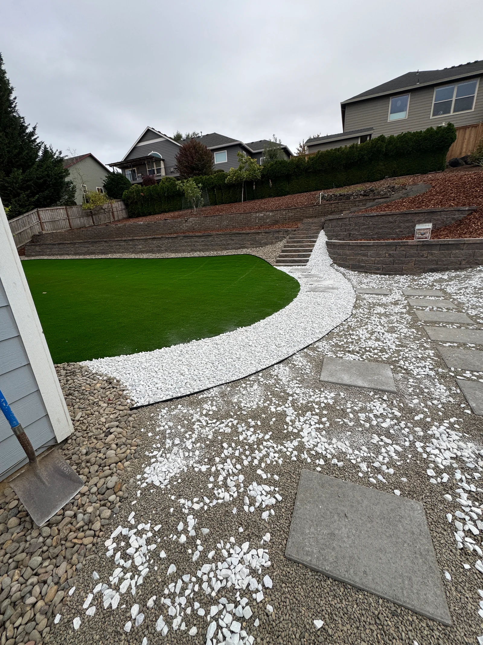 Curved paver patio with white stone accents, artificial turf, and tiered retaining walls
